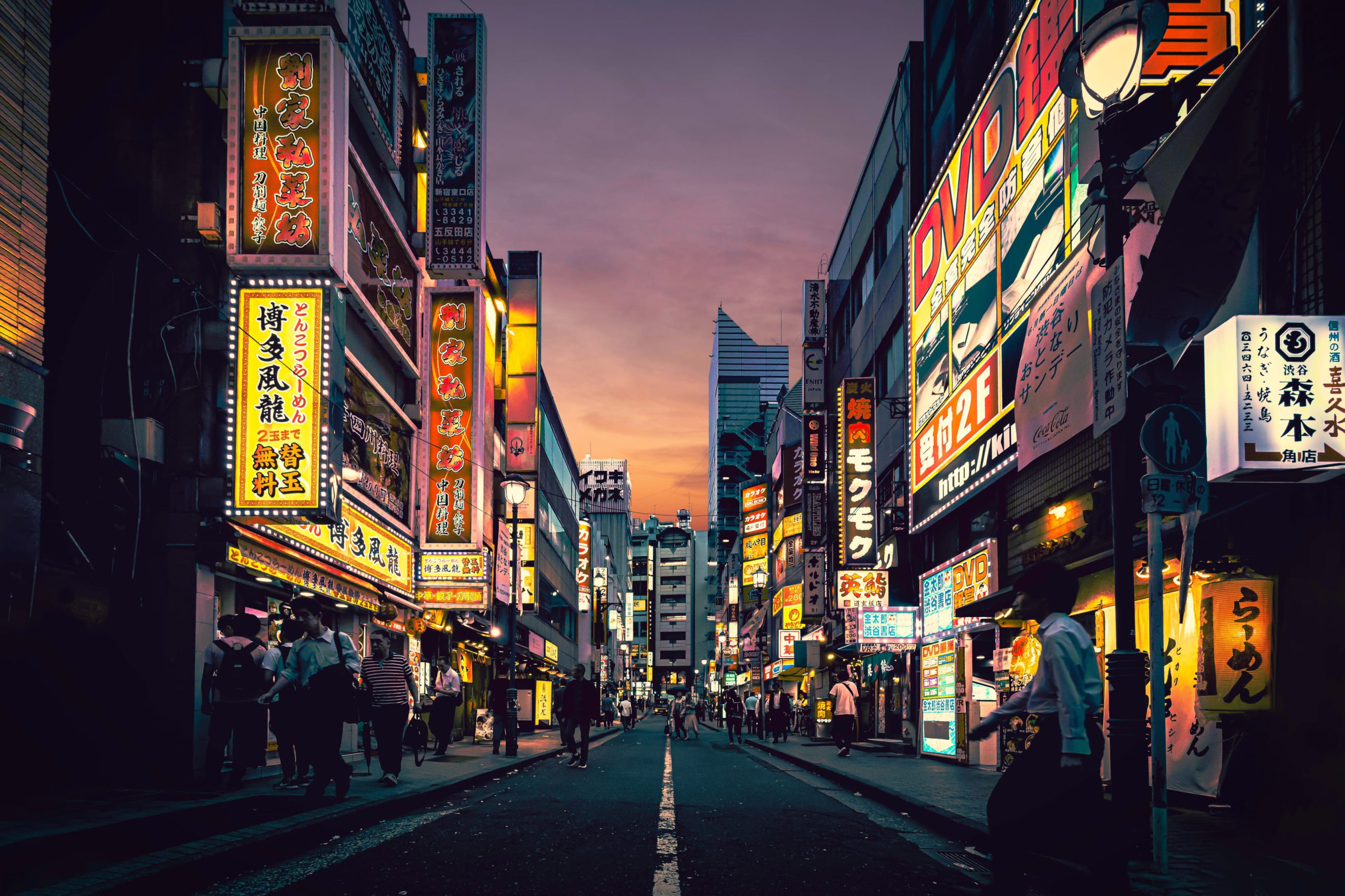 Vibrant urban street of Tokyo with neon signs illuminating the night and pedestrians strolling by.