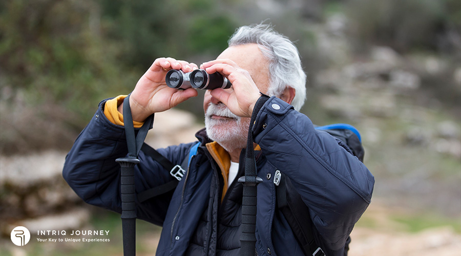 An elderly man in outdoor gear using binoculars