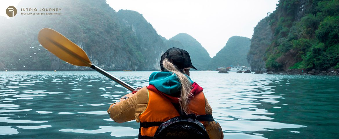 Person kayaking through scenic limestone islands in calm waters.