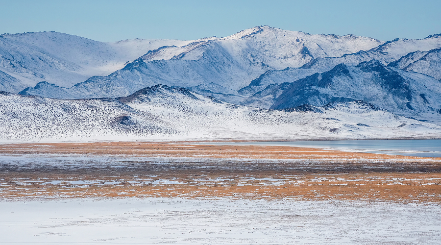 Panoramic view of snow-capped mountains and frozen steppe landscape.